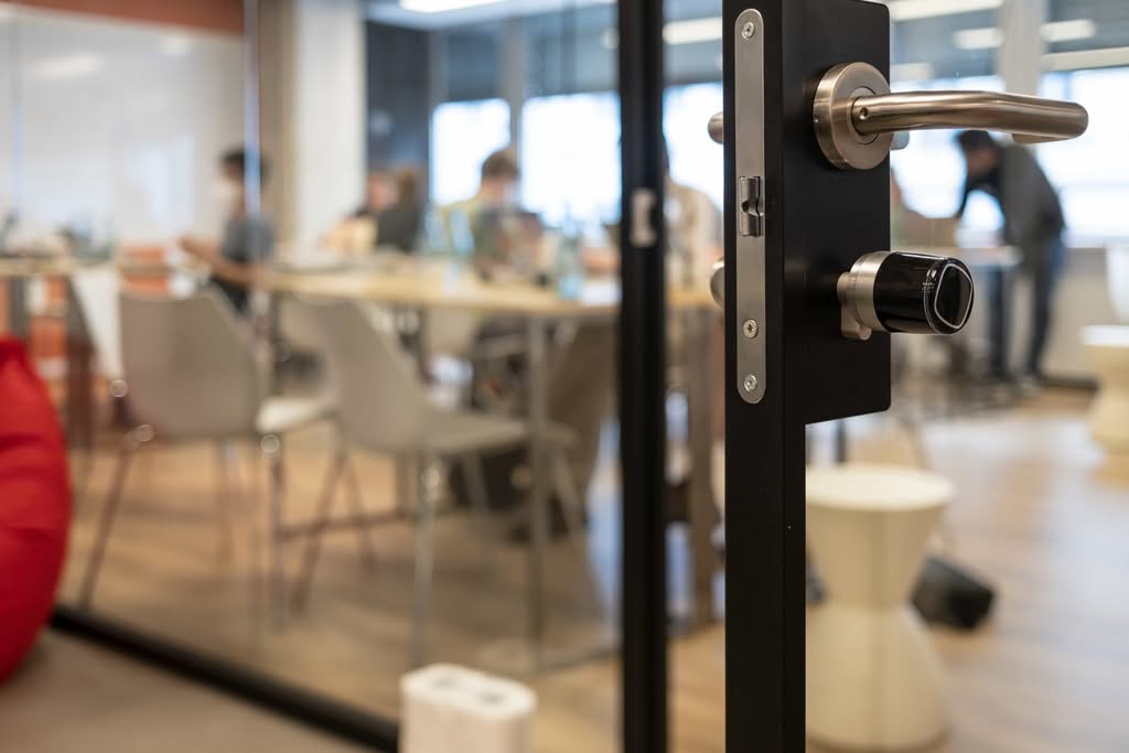 A close-up of a secure black glass door handle with a modern lock mechanism, looking into a blurred conference room where a business meeting is taking place in a HIPAA-compliant office space in Denver, Colorado.