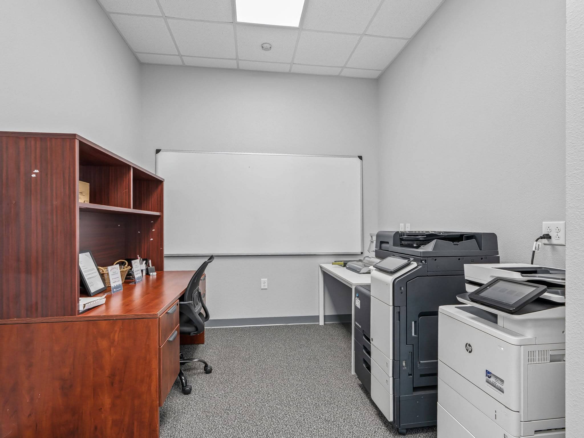 An administrative support and mail handling workroom in Ocala, FL featuring commercial printers, a large whiteboard, desktop workstation, and storage.