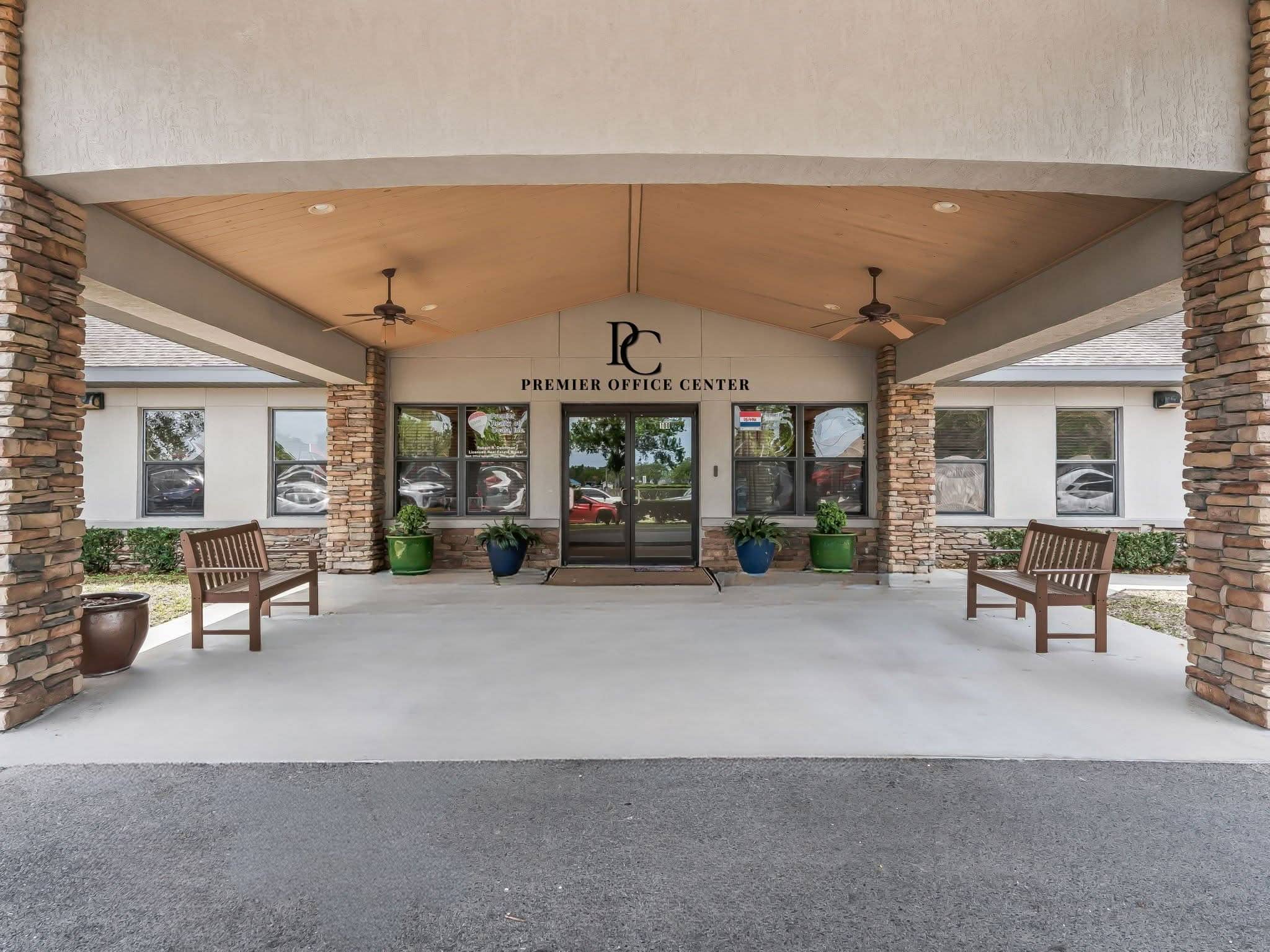 Exterior covered entrance of Premier Office Center offering flexible office space for rent in Wildwood, FL featuring stone pillars, wooden benches, and glass front doors.