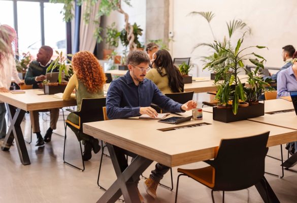 A diverse group of professionals working in a modern, plant-filled coworking space in Austin, TX, with a man in the foreground using a laptop and notebook.