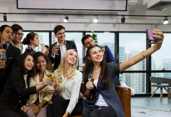 A diverse group of smiling professional colleagues taking a selfie and toasting with drinks during a corporate networking event in World Equestrian Center, Florida.