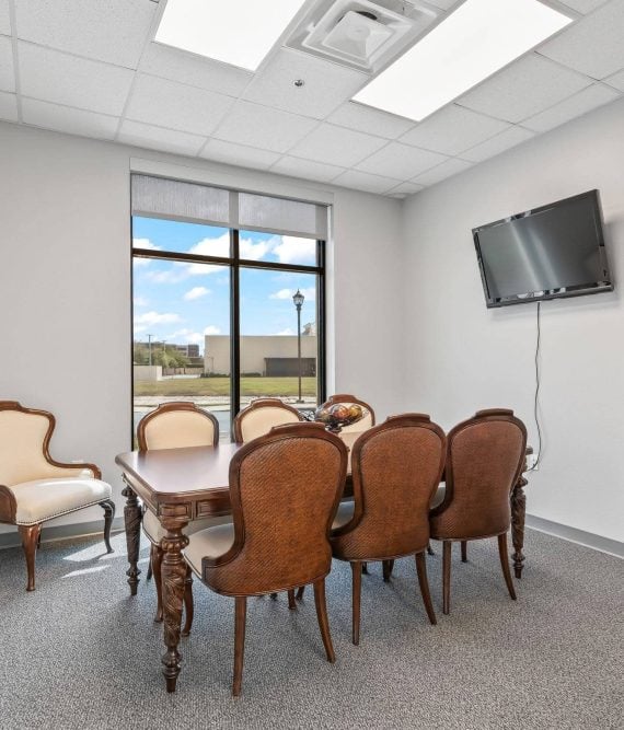 Professional executive meeting room featuring a wooden conference table, elegant upholstered chairs, a wall-mounted TV, and a large window in Wildwood, FL.