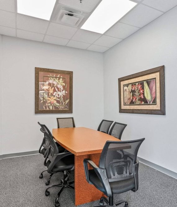 A small conference room with an wooden oval table, black mesh chairs, and framed artwork in professional office suites in Mount Dora, FL.