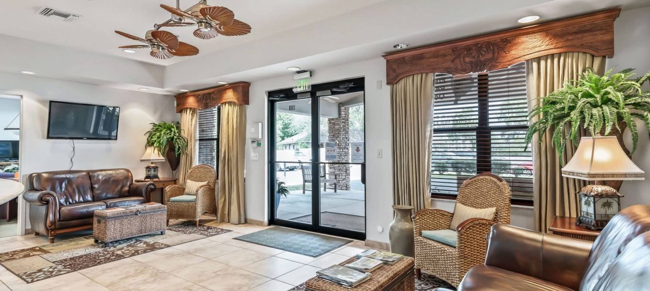 A welcoming lobby waiting area with leather sofas, woven armchairs, and ceiling fans at Premier Office Center offering professional office suites in Ocala, FL.