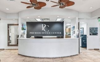 Modern reception lobby at Premier Office Center featuring a white curved front desk and logo sign for professional office suites in Wildwood, FL.
