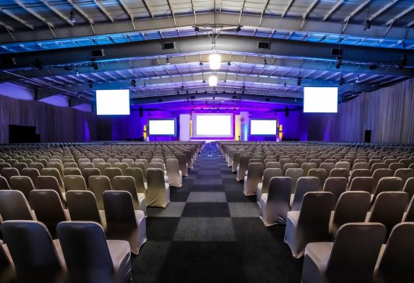 Thousands of empty chairs with white seat covers arranged in precise rows facing a large stage with blank projection screens under blue and purple ambient lighting at a training room rental facility in Wildwood, Florida.